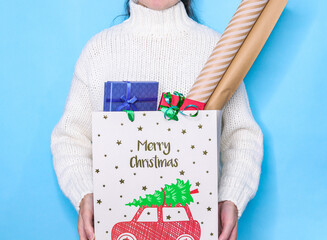 person holding christmas gift
A woman (no face) in a white knitted sweater holds a gift bag with boxes for Christmas, close-up side view.
