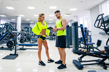 Beautiful young woman with her personal trainer at the gym discuss her progress on a clipboard held by the man. Healthy lifestyle