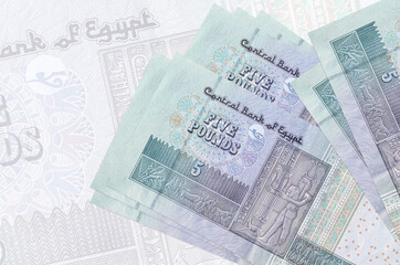5 Egyptian pounds bills lies in stack on background of big semi-transparent banknote. Abstract...