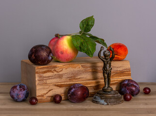 Ripe and beautiful apple with green leaves, plum and apricot on a wooden block. Gooseberries and an old bronze figurine. Still life. Vintage.