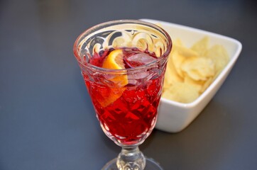 Campari soda cocktail on ice with a piece of orange  in a crystal glass, salty crackers nearby, blurred vintage background