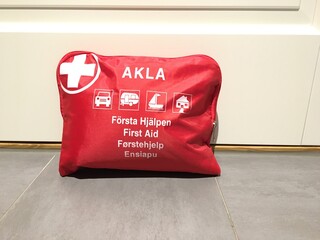 First aid kit. Red and white color. Text in Swedish, English, Danish, Norwegian and Finnish. Keep at every home.