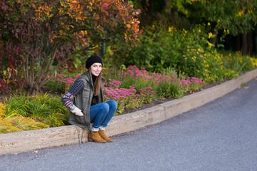 Obraz premium Full length portrait of pretty smiling young woman in casual clothes sitting on a curb during a Fall afternoon, Quebec City, Quebec, Canada