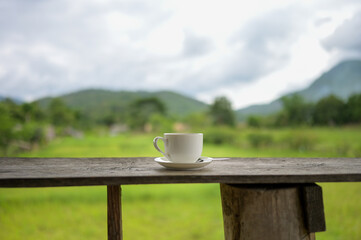 Cup of coffee or tea on a wooden table over mountains landscape and rice field with sunlight. Beauty nature background.