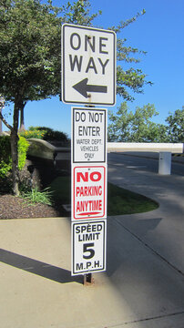 Cuatro letreros que prohíben cosas en la calle, en un solo poste indicador. Solo ida, límite de velocidad, sin estacionamiento, no ingrese.