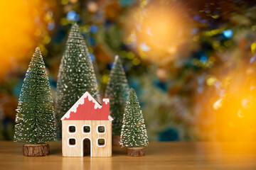 Obraz premium Christmas trees and house on wood table with bokeh background. Christmas holiday celebration and new year concept