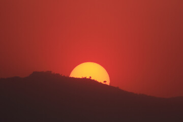Obraz premium Sun setting behind a hill with the sky turning red