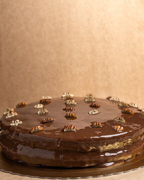 Vertical shot of a delicious cake covered in ganache and decorated with pieces of pecans