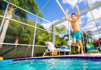 Boy jumps for joy into swimming pool on a warm summer day