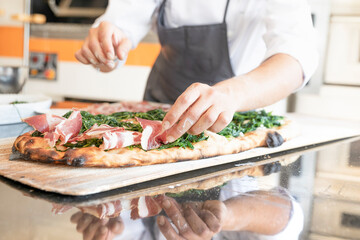 Italian cuisine: preparation of white pizza, with red ham, white mozzarella and green vegetables. Design serving. professional cook at work. food photography for menus and websites
