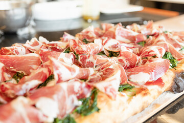 Italian cuisine: preparation of white pizza, with red ham, white mozzarella and green vegetables. Design serving. professional cook at work. food photography for menus and websites