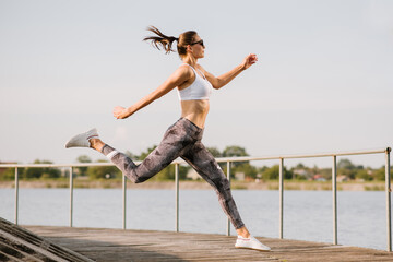 Young slim fit woman doing exercises at the lake background