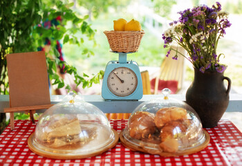 Pastries and pies on window of a bakery-coffee shop with beautiful old scales. Showcase of an street summer cafe with pastries. Croissants and buns on checkered tablecloth on terrace. Veranda decor