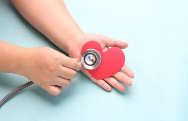 hands holding paper red heart  with stethoscope on blue background.