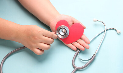 hands holding paper red heart  with stethoscope on blue background.
