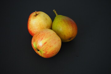 Two ripe pears and one beautiful apple. Close-up, black