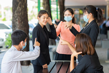 Please put on your face mask. Calling for people to wear a face mask. Group of Asian businesspeople pointing with finger on businesswoman wearing no mask.