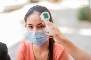 Beautiful asian woman in medical protective mask, getting her temperature check before working in office.