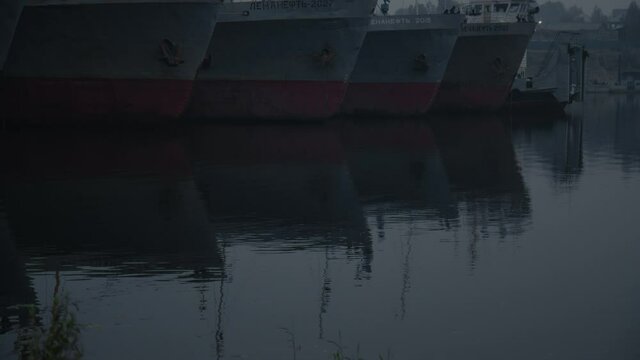 Russian ships are moored on the water at night in the dark. Old iron ships stranded at anchor, rippling water, dusk, half-light, fog. The concept of a shipyard and marine navigation. 4K
