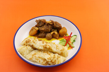 food served in round plate on orange background. in the plate have massaman beef curry and roti.