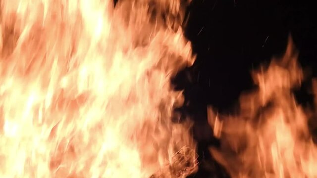 Huge solstice campfire burning in the black of night. Detail, sparks turning into flames.