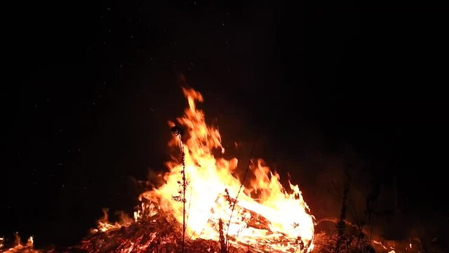 Huge solstice campfire burning in the black of night. Wideshot.