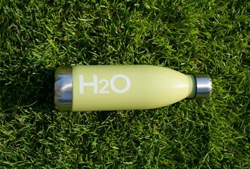 Reusable water bottle on grass background. Green refillable bottle for H2O. H2O Label. Reduce...
