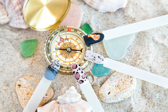 nail samples with vanile color different manicure design near a golden compass on the sand among the shells, little stones and colored pieces of glass