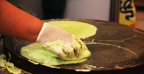 The hand man is making roti by applying the kneaded flour onto the pan and making a sheet for eating.