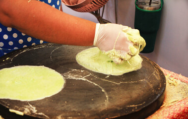The hand man is making roti by applying the kneaded flour onto the pan and making a sheet for eating.