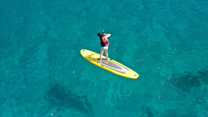 Fototapeta premium Aerial drone top down photo of unidentified woman exercising in SUP or Stand Up Paddle board in exotic island emerald beach