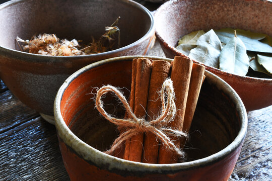 A top view image of cinnamon, dried arnica, and bay leaves in hand made pottery bowls. 