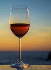 Glass with red wine, champagne against  background of  sky, dawn and  sea