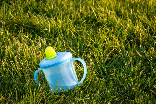 A Child's Sippy Cup Lying On The Grass And Filled With Water