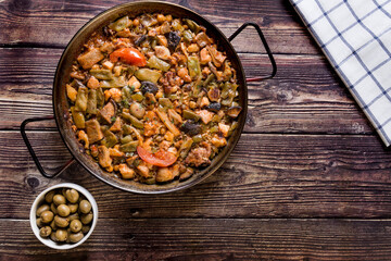 Wooden table with traditional food, vegetarian paella, green olives