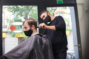 Man getting hair cut at the barber shop wearing protective mask during coronavirus pandemic