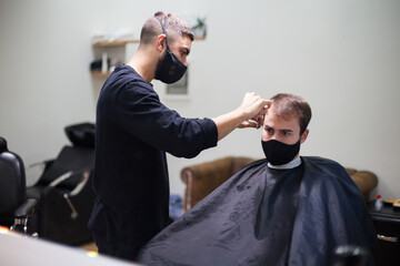 Man getting hair cut at the barber shop wearing protective mask during coronavirus pandemic