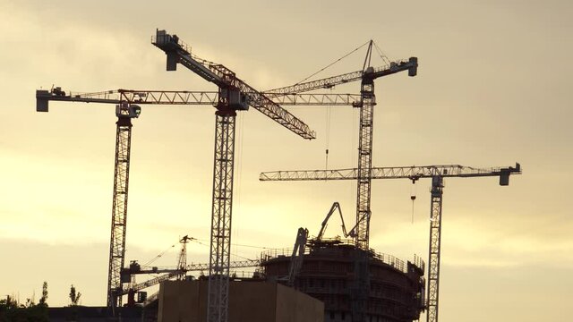 Multiple tower crane operating on a 
scaffolding construction building project at golden hour time