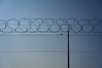 Chain-link fence with overlying barbed wire fence against a blue background. Copy-space.wide angle. Germany.