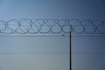 Chain-link fence with overlying barbed wire fence against a blue background. Copy-space.wide angle....