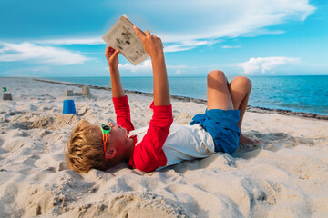 boy reading book at beach vacation, learning at sea
