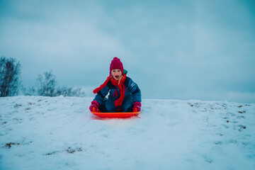 Fototapeta na wymiar happy girl sliding on sled down snow hill outdoors in winter