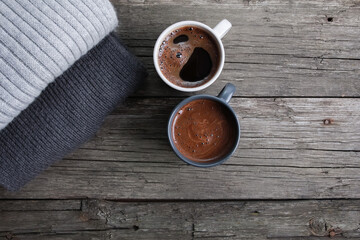 Two black coffee cups, grey folded scarfs stack on rustic old wooden boards. Copy space, top view. Autumn background, fall season, thanksgiving, dating, coffee shop menu, hot drink  concept