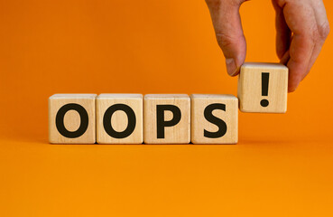 Oops sign on wooden cubes. Male hand. Beautiful orange background, copy space. Business concept.
