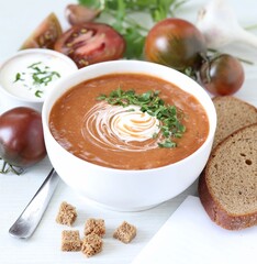 Black tomato puree soup with sour cream, croutons and parsley in a bowl on a white background