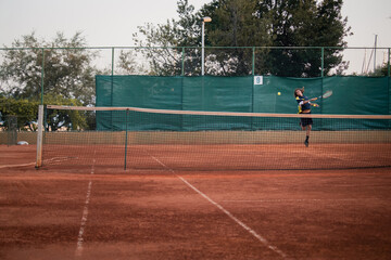 Split Croatia September 2020 Wide shot of a dirt orange tennis field, man on the other side spinning to hit the ball which is flying towards the camera