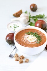 Black tomato puree soup with sour cream, croutons and parsley in a bowl on a white background