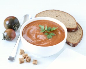 Black tomato puree soup with croutons and parsley in a bowl on a white background