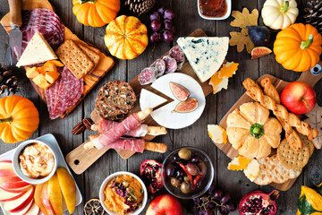 Autumn theme charcuterie table scene against a dark wood background. Variety of cheese and meat appetizers. Overhead view.