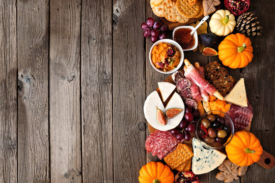 Fall theme charcuterie side border against a dark wood background. Selection of cheese and meat appetizers. Copy space.